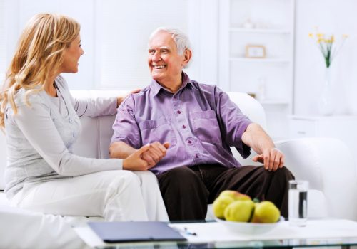 Cheerful woman sitting on the sofa with a senior man and holding his hand.